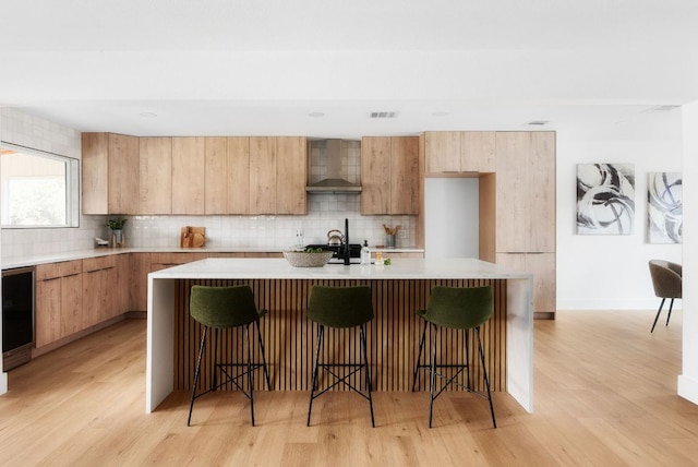 kitchen with tasteful backsplash, light countertops, wall chimney range hood, and light wood-style floors