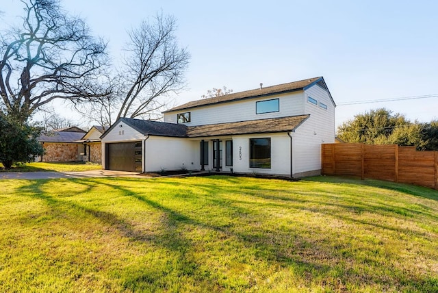 rear view of property featuring a garage, driveway, fence, and a lawn