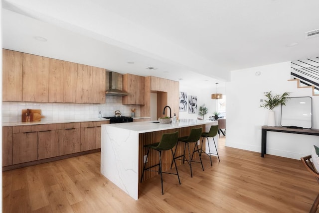 kitchen featuring wall chimney exhaust hood, backsplash, a sink, and light wood-style floors