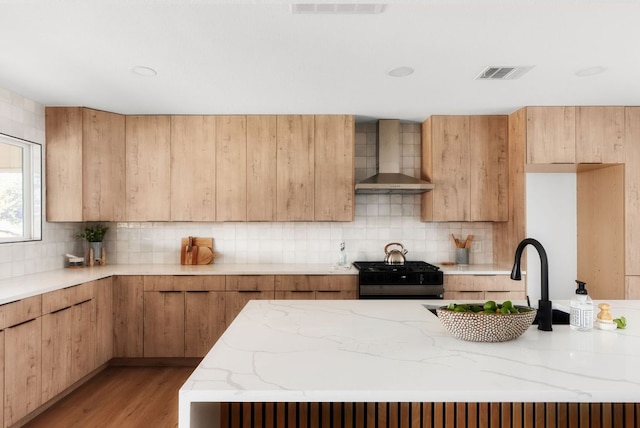 kitchen with light stone counters, visible vents, backsplash, gas stove, and wall chimney exhaust hood