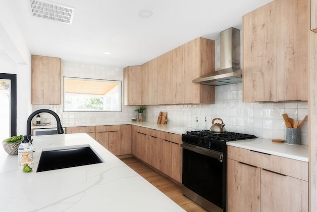 kitchen with visible vents, light brown cabinets, a sink, black gas stove, and wall chimney exhaust hood