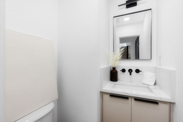 half bath with a textured wall, vanity, and toilet