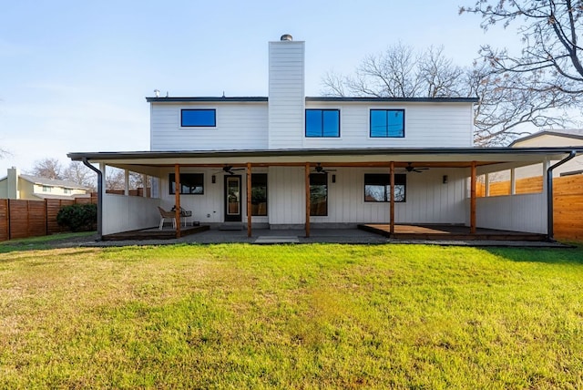 back of property with a ceiling fan, fence, a chimney, and a lawn