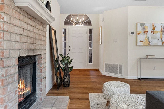 foyer featuring an inviting chandelier, wood finished floors, visible vents, baseboards, and a fireplace