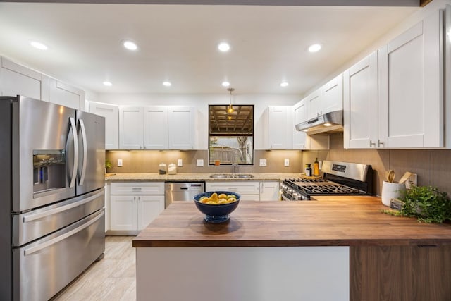 kitchen featuring appliances with stainless steel finishes, a sink, wood counters, a peninsula, and under cabinet range hood