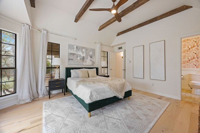 bedroom with a wainscoted wall, vaulted ceiling with beams, visible vents, light wood-style floors, and connected bathroom