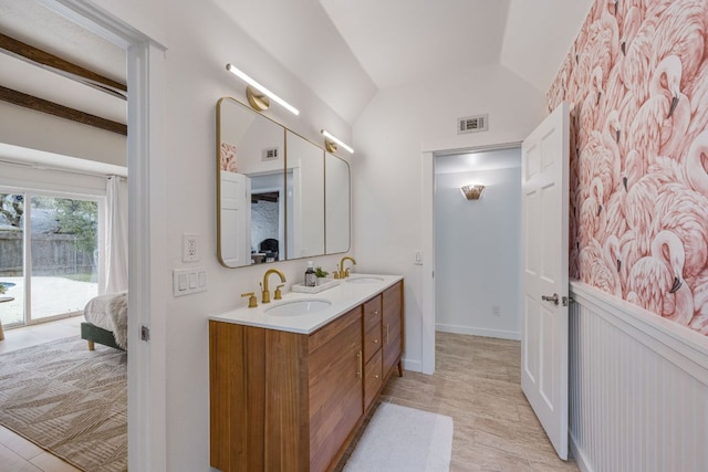 ensuite bathroom featuring connected bathroom, vaulted ceiling, visible vents, and a sink