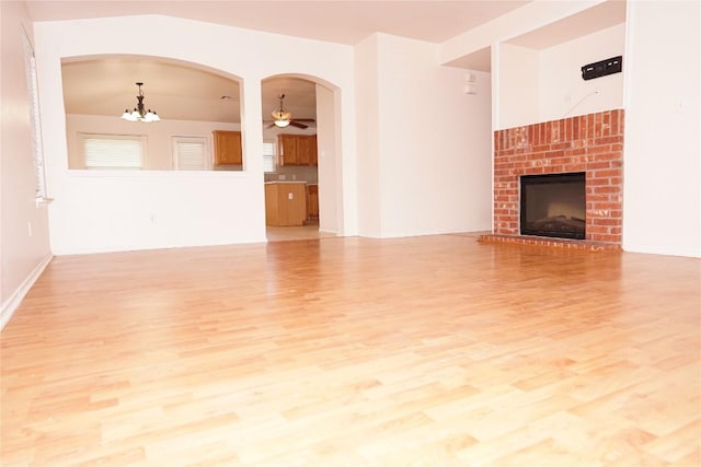 unfurnished living room featuring arched walkways, ceiling fan with notable chandelier, a fireplace, baseboards, and light wood-style floors