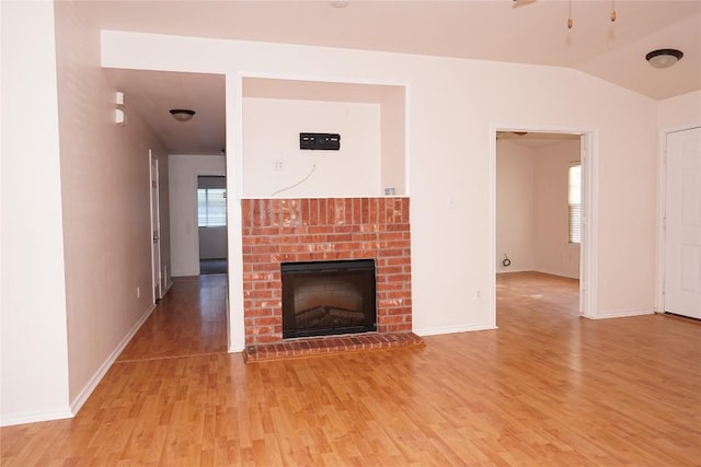 unfurnished living room with lofted ceiling, light wood-type flooring, a brick fireplace, and baseboards