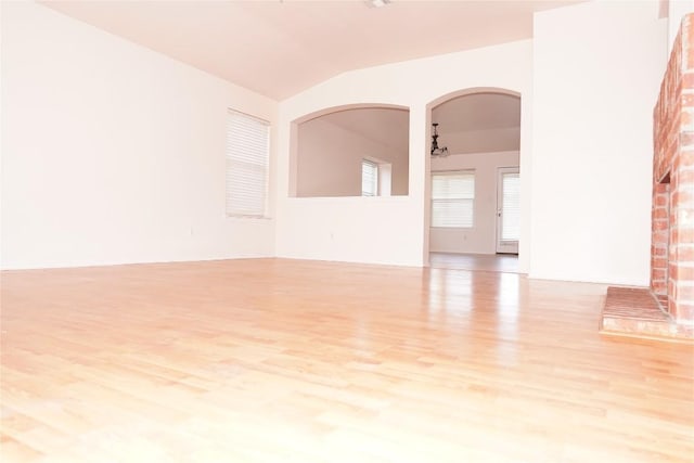 empty room featuring arched walkways, lofted ceiling, and wood finished floors