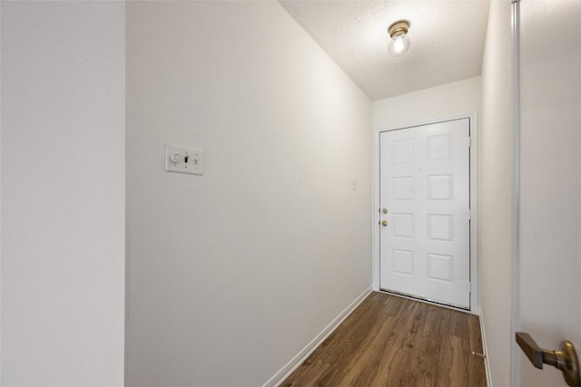 doorway to outside with a textured ceiling, dark wood-style flooring, and baseboards