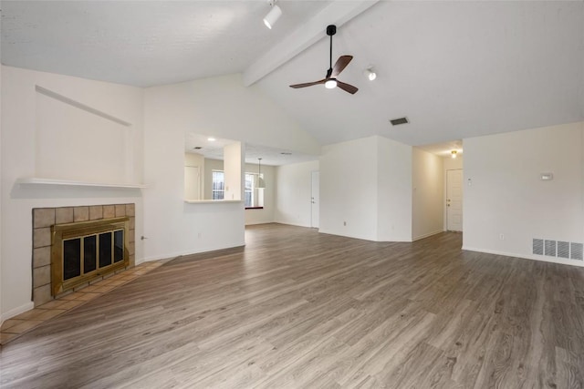 unfurnished living room with visible vents, a ceiling fan, a tiled fireplace, wood finished floors, and vaulted ceiling with beams