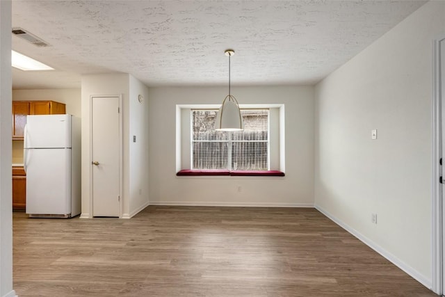 unfurnished dining area with baseboards, a textured ceiling, visible vents, and light wood-style floors