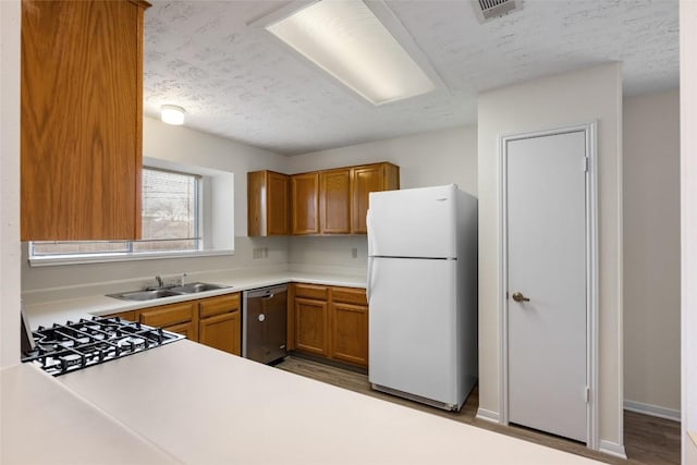 kitchen with a sink, light countertops, stainless steel dishwasher, freestanding refrigerator, and brown cabinetry