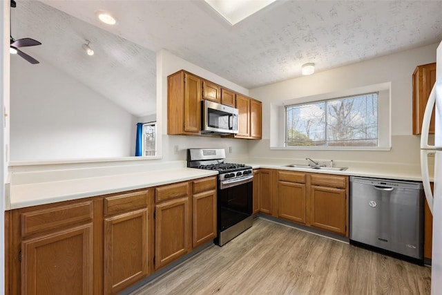 kitchen with brown cabinets, light wood-style flooring, appliances with stainless steel finishes, a sink, and a textured ceiling