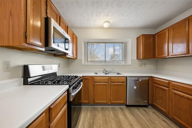 kitchen featuring appliances with stainless steel finishes, brown cabinets, light countertops, light wood-style floors, and a sink