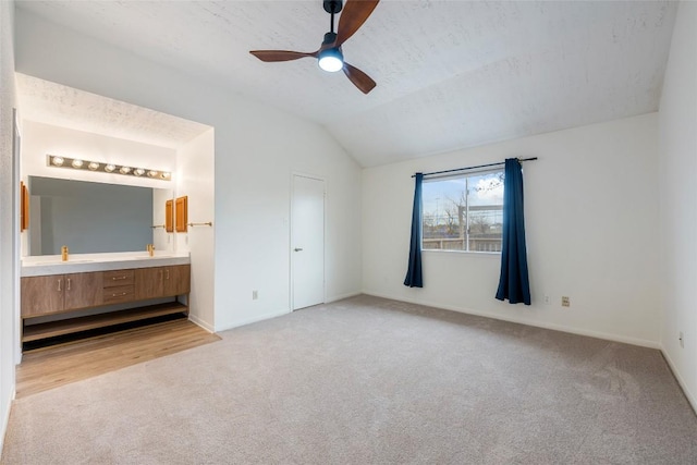 unfurnished bedroom with lofted ceiling, a ceiling fan, light carpet, connected bathroom, and baseboards