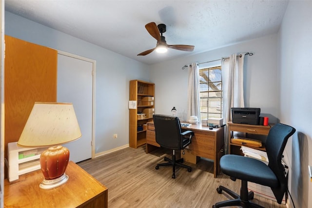 office area with light wood-type flooring, ceiling fan, and baseboards