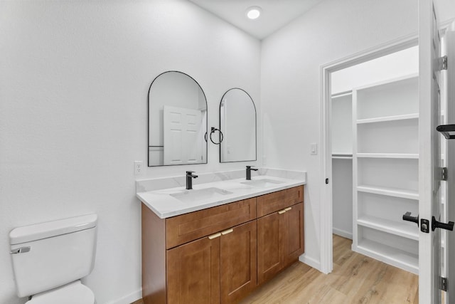 full bath featuring toilet, double vanity, a sink, and wood finished floors