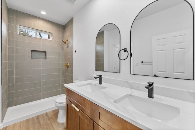 bathroom featuring tiled shower, a sink, toilet, and wood finished floors