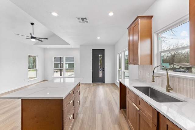 kitchen with light stone counters, brown cabinets, light wood finished floors, tasteful backsplash, and a sink