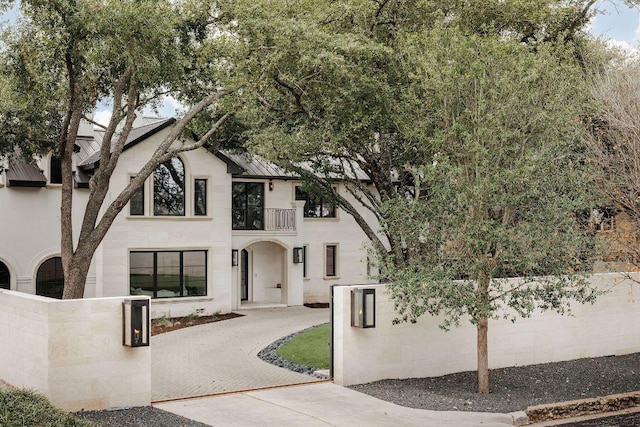 view of front facade featuring driveway, a balcony, a fenced front yard, metal roof, and a standing seam roof