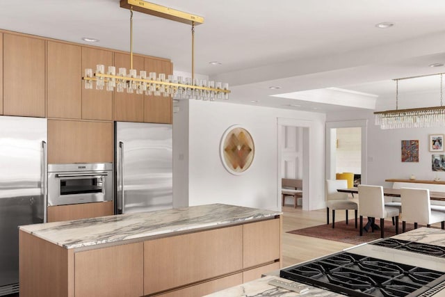 kitchen featuring light stone counters, decorative light fixtures, appliances with stainless steel finishes, light wood-style floors, and light brown cabinets