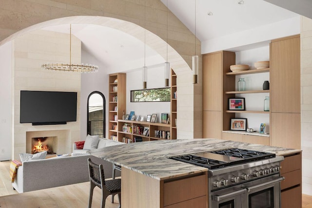 kitchen with a large fireplace, range with two ovens, lofted ceiling, light wood-style flooring, and light stone counters