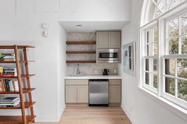 bar with a sink, baseboards, appliances with stainless steel finishes, light wood-type flooring, and tasteful backsplash