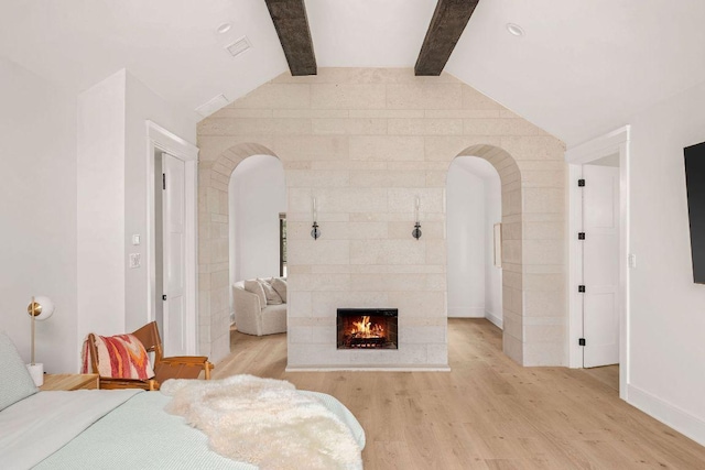 bedroom featuring lofted ceiling with beams, light wood finished floors, a fireplace, and arched walkways