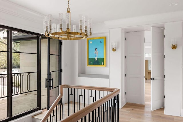 hall with light wood-type flooring, a chandelier, and an upstairs landing