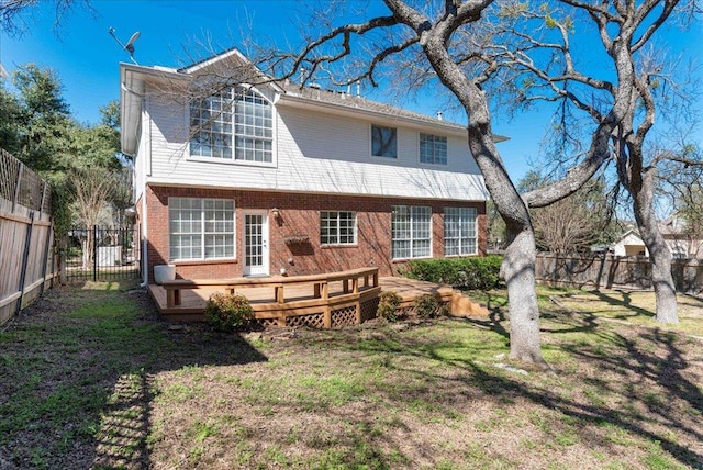 rear view of property featuring a fenced backyard, brick siding, a wooden deck, and a lawn