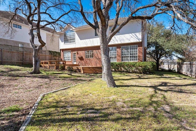 view of front facade featuring a fenced backyard, a front yard, a deck, and brick siding