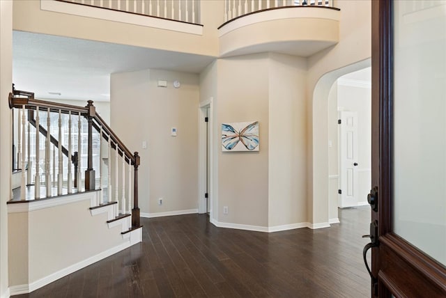 entryway with arched walkways, stairway, wood finished floors, and baseboards