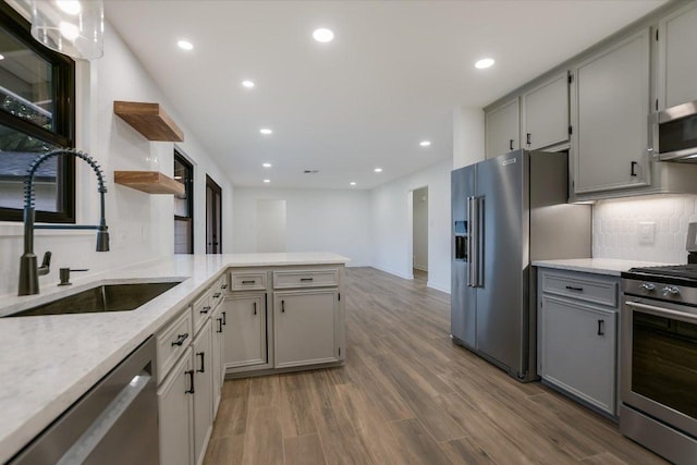 kitchen with gray cabinetry, a peninsula, a sink, appliances with stainless steel finishes, and open shelves