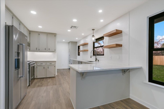 kitchen with stainless steel appliances, a peninsula, a sink, visible vents, and open shelves