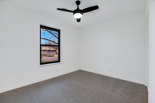 empty room featuring dark colored carpet, a ceiling fan, and baseboards