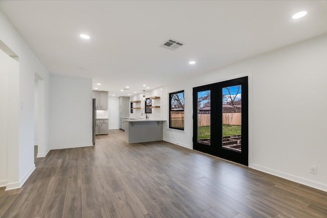 unfurnished living room with recessed lighting, dark wood-type flooring, a sink, visible vents, and baseboards