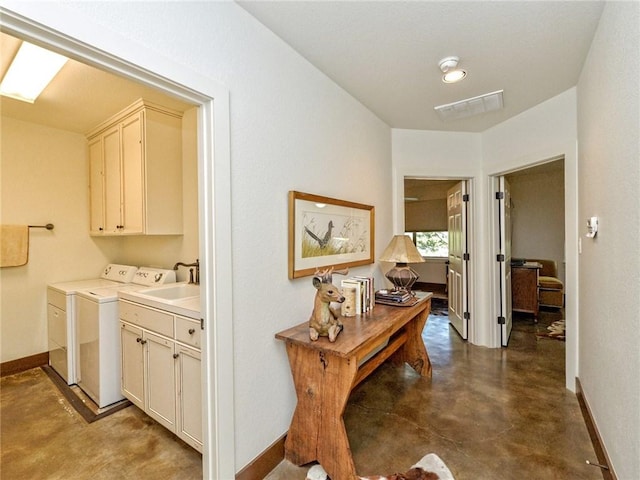 hall featuring washing machine and clothes dryer, visible vents, a sink, concrete floors, and baseboards