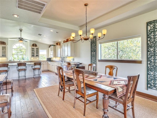 dining area featuring a tray ceiling, visible vents, hardwood / wood-style floors, baseboards, and ceiling fan with notable chandelier