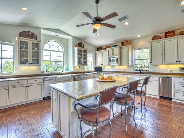 kitchen featuring a center island, dark wood-style flooring, stainless steel appliances, visible vents, and a kitchen breakfast bar