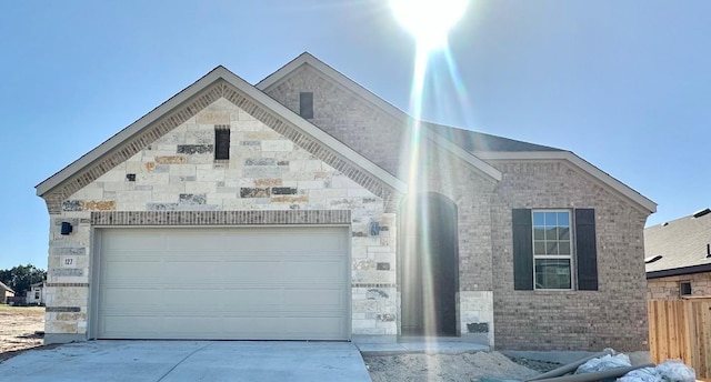 view of front of home with stone siding, fence, concrete driveway, an attached garage, and brick siding