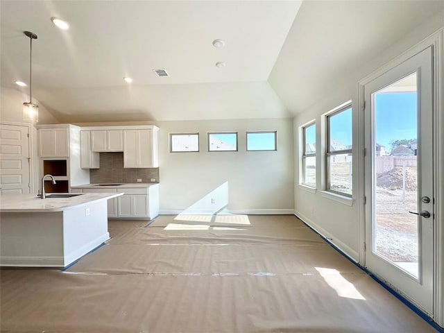 kitchen featuring visible vents, a sink, backsplash, white cabinetry, and vaulted ceiling