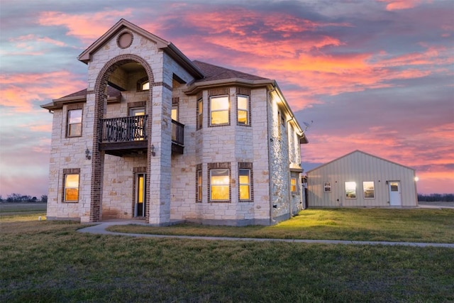 view of front of house featuring stone siding, a shingled roof, a lawn, and a balcony