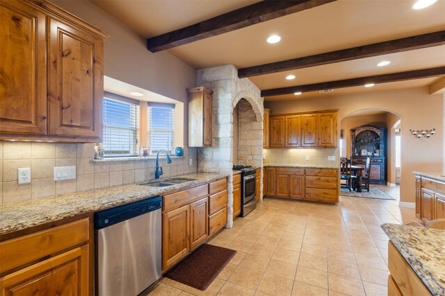 kitchen featuring arched walkways, stainless steel appliances, a sink, decorative backsplash, and brown cabinets