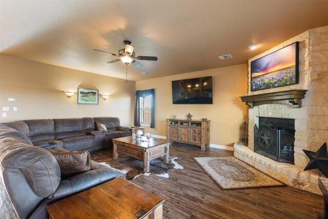 living area with baseboards, visible vents, a ceiling fan, dark wood-type flooring, and a stone fireplace