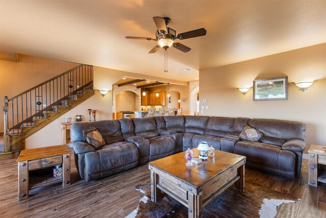 living room with stairway, a ceiling fan, arched walkways, and wood finished floors