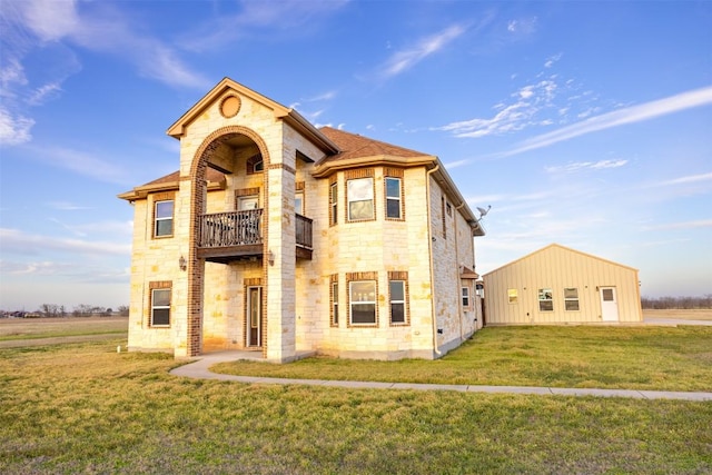 view of front of home with an outbuilding, a front yard, a balcony, stone siding, and an outdoor structure