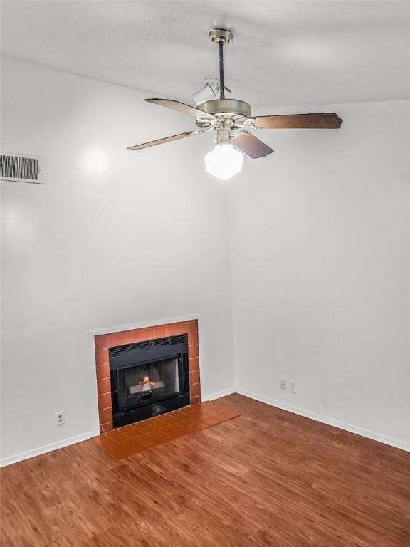 unfurnished living room with ceiling fan, wood finished floors, visible vents, baseboards, and a tiled fireplace