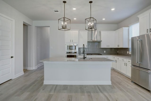 kitchen with visible vents, decorative backsplash, appliances with stainless steel finishes, wall chimney range hood, and a sink